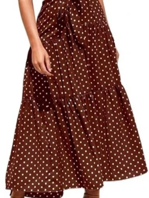 Brun prickig långklänning - Snygg brun långklänning med vita prickar och knyt i midjan. Klänningen är ärmlös och har en knapp i nacken. Perfekt för dig som gillar retrovibbar och vill ha en luftig och bekväm stil.