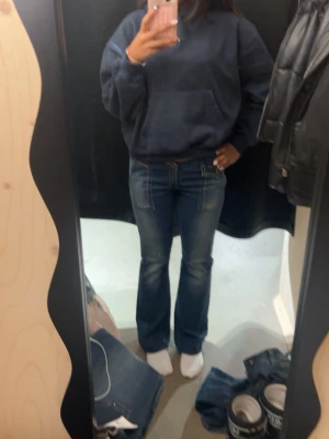 Blå bootcut jeans med kontrastsömmar - Säljer ett par blå bootcut jeans med snygga kontrastsömmar och klassiska fickor både fram och bak. Jeansen har en låg midja och är tillverkade i stretchigt denim för skön passform. Perfekta till en avslappnad streetstyle-look.