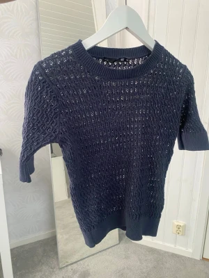 Mörkblå stickad topp från 157 - Säljer en mörkblå stickad topp från 157 i storlek XS. Tröjan har korta ärmar, rund halsringning och  hålmönster över hela tröjan 
