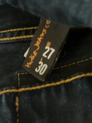 Mörkblå skinny jeans från Nudie Jeans - Snygga mörkblå skinny jeans från Nudie Jeans med klassiska orangea sömmar. Modellen har smal passform och normal midja. Tillverkade i stretchigt denim för en bekväm känsla. Perfekta för dig som gillar en stilren och tidlös look.