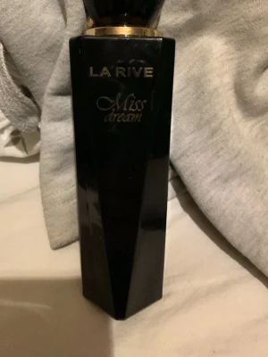 La Rive Miss Dream parfym - Snygg parfymflaska från La Rive i modellen Miss Dream. Flaskan är svart med guldiga detaljer och har en elegant, kantig form. Perfekt för dig som gillar stilrena och lyxiga dofter.