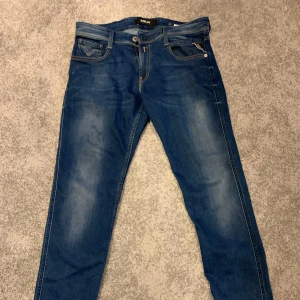 Blå jeans från Replay - Säljer ett par snygga blå jeans från Replay, modell Anbass. De har en klassisk femficksdesign och är i mycket bra skick. Perfekta för både vardag och fest! Passformen är slim och de har en bekväm midwaist. Sköna och stilrena jeans som passar till allt. De är använda fåtal gånger och ny pris är 1100kr mitt pris 400kr 