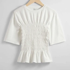 Other stories trendig tröja - Säljer en superfin vit topp med smockdetaljer i midjan som ger en snygg passform. Toppen har korta ärmar och en liten volang vid nederkanten.       Köpt för 390 kr på other stories, använd endast två gånger💞