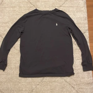 Svart långärmad tröja från Ralph Lauren - Säljer en stilren svart långärmad tröja från Ralph Lauren med deras ikoniska logga broderad på bröstet. Perfekt för både vardag och finare middagar . Tröjan är i mycket bra skick och passar till alla tillfällen. Skön och enkel att matcha med andra plagg.