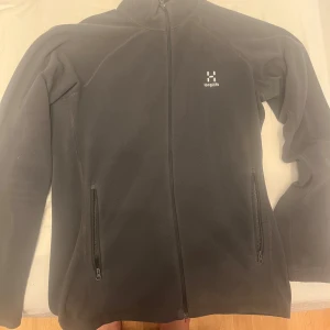 Svart fleece tröjan från Haglöfs - Säljer en grå fleece tröjan från Haglöfs i mycket bra skick. Den har en dragkedja framtill och två praktiska fickor med dragkedjor. Perfekt för kyliga höst- och vinterdagar. Tröjan är långärmad och supermjuk, vilket gör den både bekväm och varm. Passar perfekt för utomhusaktiviteter eller mysiga hemmakvällar.