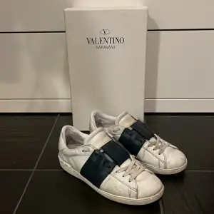 Säljer ett par snygga Valentino Garavani sneakers i vitt med breda mörkblå detaljer. Skorna har en stilren design med snörning och är i bra skick. Perfekta för både vardag och festliga tillfällen. Kommer med originalkartong.