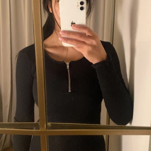 Svart ribbad tröja med dragkedja - Säljer en svart ribbad tröja med lång ärm och en snygg dragkedja framtill. Perfekt för både vardag och fest! Tröjan är tight och framhäver figuren på ett stilrent sätt. Passar bra till jeans eller kjol för en komplett look.