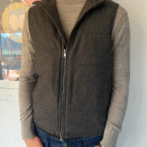 Quiltad ullväst från Oscar Jacobson - Snygg mörkgrå väst, modell Liner,  i 100% ull från Oscar Jacobson. Använd endast ett fåtal gånger så i nyskick. Västen har en dragkedja framtill och är quiltad för extra värme. Vadderad. Perfekt för höst och vår eller fina vinterdagar med stickad tröja under. Sidfickor med dragkedja. Storlek 48. 