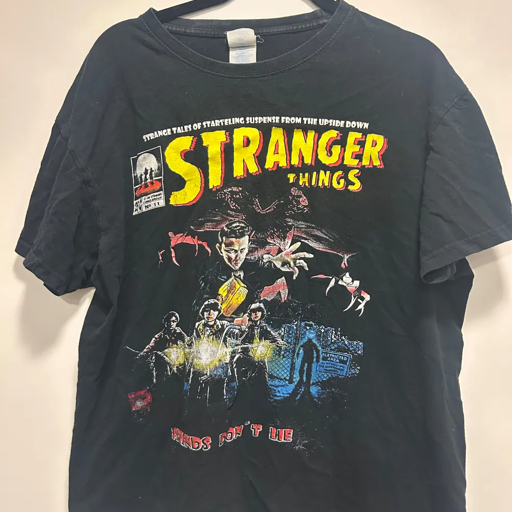 Cool svart t-shirt med Stranger Things-tryck i rött och gult. Perfekt för fans av serien! Den har korta ärmar och är gjord i bomull, vilket gör den bekväm att bära. Passar bra till vardags eller för en avslappnad look.. T-shirts.