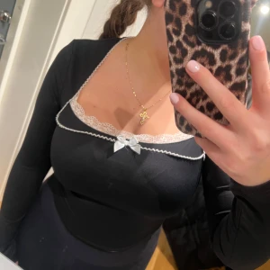 Svart långärmad topp med spetsdetaljer - Säljer en elegant svart långärmad topp med vacker spetskant vid halsringningen och en söt liten rosett framtill. Perfekt för både vardag och festliga tillfällen. Toppen har en tight passform som framhäver figuren. Aldrig använd endast provad 