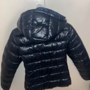 Blå pufferjacka med huva - Säljer en blå jacka från lager157  i nytt skick. Aldrig använd och passar inte på mig, kan inte skicka tillbaka den då jag råka ta bort lappen i jackan. Jackan har en dragkedja framtill och en praktisk huva. Perfekt för kalla höst- och vinterdagar. Den är långärmad och har en glansig yta som ger en stilren look. Passar både till vardags och lite finare tillfällen.