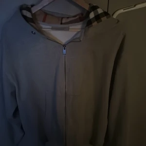Grå hoodie från Burberry - Säljer en snygg grå hoodie från Burberry med klassiskt rutigt mönster i huvan. Den har en dragkedja framtill och är perfekt för höst och vår. Passar både till vardags och lite finare tillfällen. Storleken är M, Cond: 10/10! Använd endast max 2-3 gånger. Pris kan diskuteras vid snabb affär!🔥