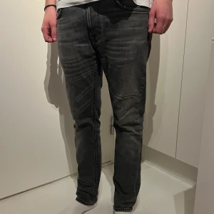 Grå jeansbyxor - Säljer ett par grå jeans från nudie i bra skick! Dem har lite slitningar och är i modellen lean dean storlek 31/30 personen på bilden är 183cm