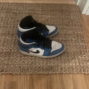 Nike Air Jordans i blått och vitt - Säljer ett par Nike Air Jordans i blått och vitt. Skorna har en klassisk design med svart snörning och Nike-logga på sidan. Perfekta för både vardag och sportiga tillfällen. De är i bra skick och redo för nya äventyr!