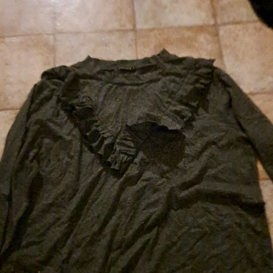 Mörkgrå tröja med volangdetaljer från Rut&Circle - Säljer en snygg mörkgrå tröja från Rut&Circle i storlek L. Tröjan har långa ärmar och en fin volangdetalj framtill som ger en extra touch. Perfekt för höst och vinter!OBS den är liten i storleken