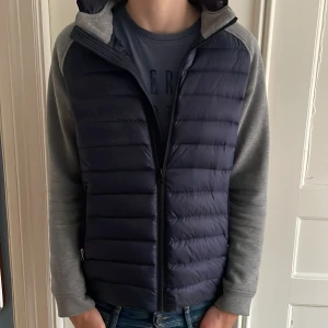  Cardigan från Boggi Milano - Säljer en snygg blå pufferjacka från Boggi Milano i storlek M. Jackan har gråa ärmar och en praktisk dragkedja framtill. Perfekt för höst och vår med sin stilrena design och bekväma passform. Huvan ger extra skydd mot väder och vind. Passar både till vardags och lite finare tillfällen. Steal!!🚨🚨