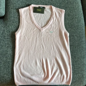 Ljusrosa väst från Giorgio Armani - Säljer en stilren ljusrosa väst från Giorgio Armani. Den är v-ringad och har en liten broderad logga på bröstet. Perfekt för vår och sommar, och kan enkelt matchas med en skjorta eller t-shirt. Västen är i mycket bra skick och ger en elegant touch till din outfit.