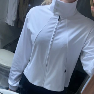 Vit jacka från J.Lindeberg - Säljer en stilren vit jacka från J.Lindeberg i mycket bra skick. Jackan har en hög krage och dragkedja framtill. Perfekt för vår och höst, med en normal passform och långa ärmar. Enkelt att matcha med olika outfits! Går att använda till golf och tennis, även som en vardaglig tröja. Finns inte i ordinarie sortiment då det är ett sampel, ingen som har likadan🙌