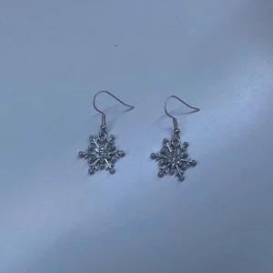 Silvriga snöflingeörhängen - Säljer ett par superfina silvriga örhängen formade som snöflingor. Perfekta för vintern och julens alla fester! De är i mycket bra skick och har en glittrig yta som fångar ljuset fint. Passar perfekt till både vardag och festliga tillfällen. ❄️✨