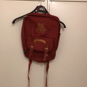 Röd ryggsäck med Hogwarts-emblem - Säljer en snygg röd ryggsäck med Hogwarts-emblem på framsidan. Den har ett stort huvudfack och en mindre ficka med spännen. Perfekt för skolan eller som en cool accessoar för Harry Potter-fans! 🧙‍♂️