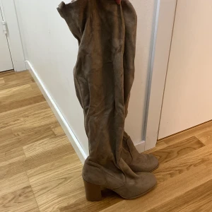 Beige mockastövlar med klack - Säljer ett par snygga beige stövlar i mocka med hög klack och dragkedja på sidan. Perfekta för höst och vinter, dessa stövlar är både stiliga och bekväma. De har en spetsig tå och är i mycket bra skick. Helt nya! 