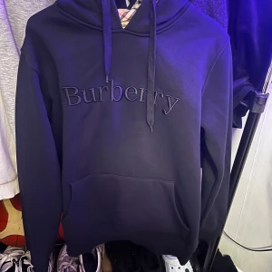 Svart hoodie från Burberry inte äkta! - Säljer en stilren svart hoodie från Burberry med klassiskt rutigt mönster i huvan. Tröjan har en broderad Burberry-logga på framsidan och en bekväm passform. Perfekt för både vardag och lite finare tillfällen. 🖤