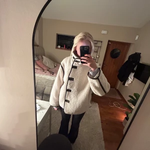 Vit teddyjacka med svarta detaljer - Mysig vit teddyjacka med svarta knappar och detaljer. Perfekt för kyliga dagar, den har en avslappnad passform och långa ärmar. Jackan är nästan helt ny🩷