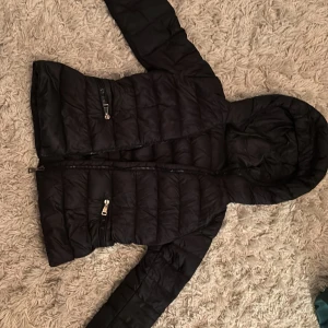 Svart dunjacka från Moncler - Säljer en snygg svart dunjacka från Moncler i mycket bra skick. Jackan har en huva och dragkedja framtill.Det fanns ett hål på armen så har sytt på en liten lapp men syns knappt finns bild på det 