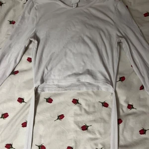 Vit långärmad topp med knytband - Säljer en vit långärmad topp i bomull med knytband i midjan. Perfekt för en avslappnad stil eller att klä upp med accessoarer. Toppen är i bra skick och passar till både vardag och fest. Har ett läppsift märke i halsen men syns inte när den väl sitter på!