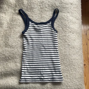 Randig ribbad linnetopp - Säljer en snygg randig linnetopp i ribbat material. Den är vit med svarta ränder och har en tight passform. Perfekt för sommardagar eller som ett basplagg i garderoben. Toppen är i bra skick men sömnen har gått upp lite ner vid kanten. 
