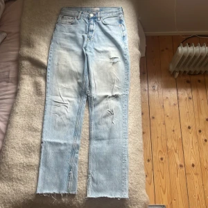 Ljusa jeans med slitningar - Säljer ett par ljusa jeans i bra skick med slitningar framme och bak. De har en straight passform och en medelhög midja. Jeansen är avklippta och har sluttar längst mera vid fötterna. På mig som är 165 sitter jeansen precis vid fötterna men inte hela vägen ner till marken.
