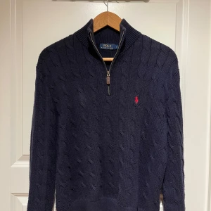 Mörkblå stickad tröja från Polo Ralph Lauren - Säljer en snygg mörkblå stickad tröja från Polo Ralph Lauren. Den har en dragkedja vid halsen och det klassiska röda logotypbroderiet på bröstet. Perfekt för kyliga dagar och ger en stilren look. Passar både till vardags och lite finare tillfällen.
