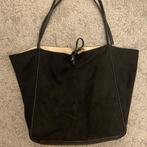 Svart axelväska från H&M - Säljer en stilren svart axelväska från H&M. Väskan är rymlig och perfekt för vardagsbruk. Den har långa handtag och en enkel knytning upptill. Passar till alla tillfällen och är lätt att matcha med olika outfits.