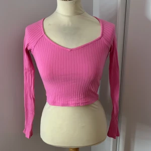 Rosa ribbad croppad topp - Säljer en superfin rosa ribbad topp med långärmad design. Den är croppad och har en snygg v-ringad hals. Perfekt för både vardag och fest! Passar bra till jeans eller kjol för en trendig look. 💖