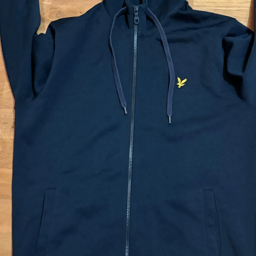 Säljer en snygg mörkblå hoodie från Lyle & Scott i storlek L men passar även M. Den har en dragkedja framtill och en liten gul logga på bröstet. Perfekt för höst och vinter, och den är superbekväm med långa ärmar och en praktisk huva. Passar både till vardags och chillkvällar. 🧢. Tröjor & Koftor.