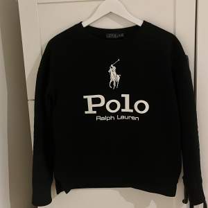 Säljer en snygg svart tröja från Ralph Lauren med deras ikoniska logga i vitt på framsidan. Tröjan har långa ärmar och är perfekt för en stilren look. Passar både till vardags och fest. Skön och bekväm att ha på sig! Liten i storleken