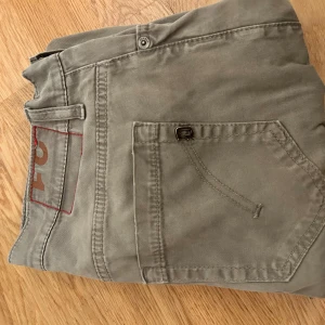 Grå/gröna byxor från Dondup - Säljer ett par snygga byxor från Dondup. De har en klassisk design med normal passform och är perfekta för både vardag och fest. Byxorna har knappar och en dragkedja framtill. De är i mycket bra sick 9,5/10. Passformen är perfekt för dig som vill ha den inte för tajt men ändå inte pösiga. Passar till många outfits.