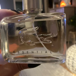 Essential parfym - Säljer en stilren och fräsch parfym från Lacoste, modellen Essential. Flaskan är genomskinlig med en silverfärgad kork och har den ikoniska krokodilen ingraverad. Perfekt för vardagsbruk eller speciella tillfällen. Doften är lätt och uppfriskande, perfekt för dig som gillar en sportig och elegant stil. 75 ml