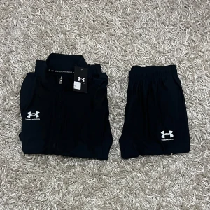 Under Armour tracksuit - Säljer en Under Armour tracksuit i storlek M. Tracksuiten består av en långärmad jacka med dragkedja och matchande byxor. Perfekt för träning eller en avslappnad dag. Materialet är mjukt och bekvämt, vilket gör det idealiskt för både inomhus och utomhusaktiviteter.(KVITTO FINNS)