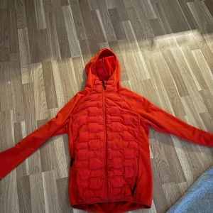 Röd pufferjacka med huva - Snygg röd pufferjacka med huva och dragkedja framtill. Jackan har långa ärmar och quiltade detaljer på framsidan och baksidan. Perfekt för kyligare dagar.