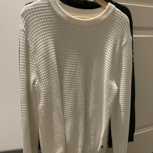 J.Lindeberg  tröja - Säljer en stilren vit stickad tröja med ett rutigt mönster. Tröjan har långa ärmar och en rund halsringning. Perfekt för kyligare dagar.