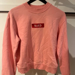 Rosa sweatshirt från NA-KD - Säljer en snygg rosa sweatshirt från NA-KD med deras logga framtill. Tröjan har långa ärmar och ribbade muddar vid ärmslut och nederkant. Perfekt för en avslappnad stil. Storlek M men skulle säga att den är mer S. 