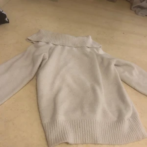 Beige stickad tröja från Lindex - Mysig beige stickad tröja från Lindex för barn i storlek 146/152. Tröjan har en bred krage och långa ärmar, perfekt för kyliga dagar. Den ribbade strukturen ger en extra touch av stil.