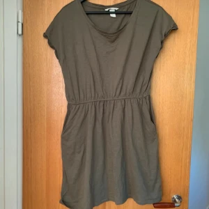 Grön kortärmad klänning - Säljer en enkel och stilren grön klänning med korta ärmar. Klänningen har en elastisk midja som ger en smickrande passform. Perfekt för en avslappnad look.