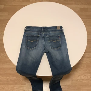 Blå jeans från Replay - Snygga blå jeans från Replay med klassisk femficksdesign och ljusa slitningar. De har en knappgylf och märkeslogga på bakfickan. Perfekta för en avslappnad stil.