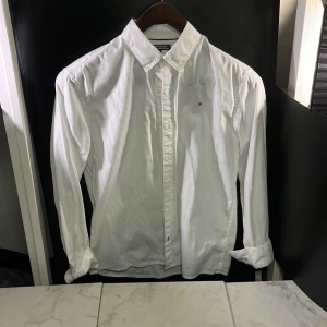 Vit skjorta från Tommy Hilfiger - Klassisk vit skjorta från Tommy Hilfiger med knappar och långärmad design. Perfekt för en stilren look. Tillverkad i ett bekvämt material som passar till många tillfällen. Hör av er vid minsta fundering🙌