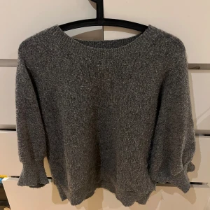 Grå stickad tröja från Lindex - Mysig grå stickad tröja från Lindex med volangdetaljer vid ärmslut och nederkant. Perfekt för kyliga dagar. Den har trekvartsärmar! Passar mig som har S. Köpte den för 249kr säljer den för 100+frakt 
