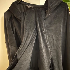 Svart långärmad mjukis med byxor - Elegant svart tröja med luva  med långa ärmar & byxor. Settet har en unik design med draperade detaljer framtill och en mjuk, bekväm passform. Perfekt för en stilfull look.