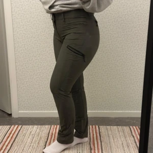 Gröna vandringbyxor, McKinley - Snygga gröna vandringsbyxor från McKinley med ganska tight passform. Byxorna har praktisk dragkedja ena sidan och är perfekta för en stilren look. De är tillverkade i ett bekvämt material som ger extremt bra rörelsefrihet! 