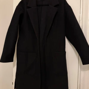 Svart kappa från Pieces - Elegant svart kappa från Pieces med klassisk design. Den har långa ärmar och en stilren siluett, perfekt för kyligare dagar. Kappan har en enkel och tidlös look som passar till många olika outfits.